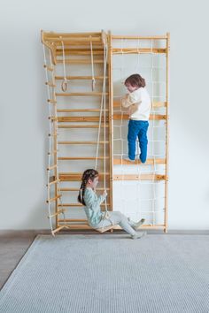 two children are playing in a room with wooden shelves and ladders on the wall