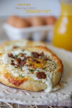 a close up of a small pizza on a plate with eggs in the back ground