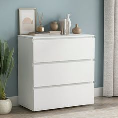 a white chest of drawers next to a potted plant in a room with blue walls