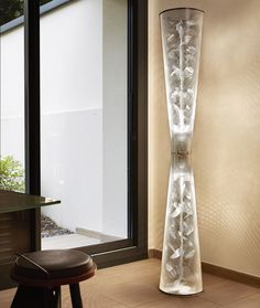 a tall glass vase sitting on top of a hard wood floor next to a window