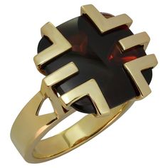 This gorgeous Cartier cocktail ring is crafted in 18k yellow gold and features a cabochon garnet set in a geometric crown. The 14.7mm x 14.9mm buff-top cushion-shaped garnet has dark red color with brownish tones, a fairly good transparency with some inclusion visible upon close inspection, and surface wear in form of fine scratches visible upon close inspection. Made in France circa 1970s. Measurements: 0.66" (17mm) width, 0.66" (17mm) length. The ring size is 6.25 - EU 53. Resizable. Sizing fees will be provided upon request. Modern Gold Signet Ring With Cabochon, Modern Gold Oval Ruby Ring, Modern Oval Ruby Ring In Gold, Modern Oval Gold Ruby Ring, Modern Yellow Gold Signet Ring With Cabochon, Modern Yellow Gold Ruby Ring For Formal Events, Modern Yellow Gold Ruby Ring For Formal Occasions, Luxury Yellow Gold Rings With Garnet, Modern Yellow Gold Ruby Ring With Polished Finish