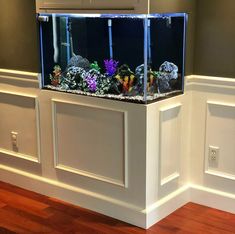 an aquarium in the corner of a room with wood floors and walls, along with white paneling