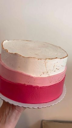 a person holding a cake with pink and white frosting on it's side