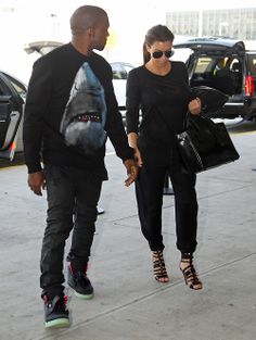 a man and woman walking down the street holding hands with one another while wearing sunglasses