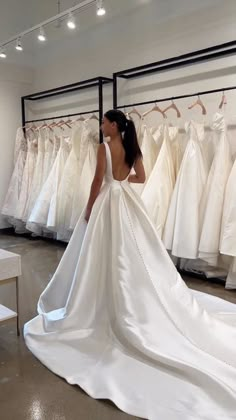 a woman standing in front of a rack of wedding dresses