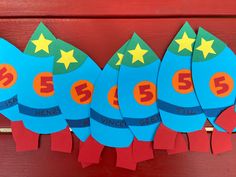 four paper rockets with numbers and stars on them hanging from a red wooden wall