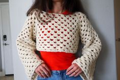 a woman standing in front of a wall wearing a crocheted sweater