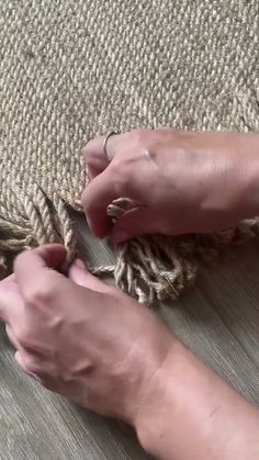 two hands are working on a rug that is being made from wood and jute