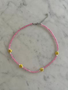 the pink and yellow beaded bracelet with smiley faces is on top of a marble surface