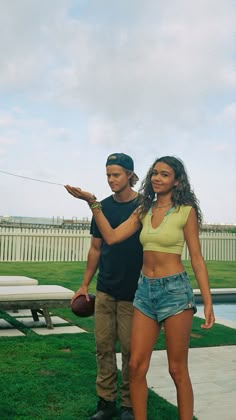 a man and woman standing next to each other in front of a bench on the grass