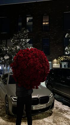 a person holding a bunch of red flowers in front of a car on the street