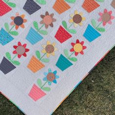 a patchwork quilt with flower pots on the front and back, sitting in grass