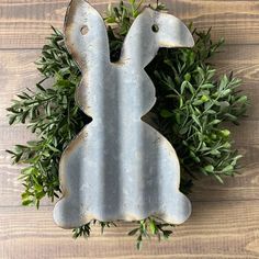 a metal rabbit shaped object sitting on top of a wooden table next to green plants