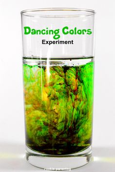 a glass filled with green liquid on top of a white table next to a sign that says dancing colors experiment