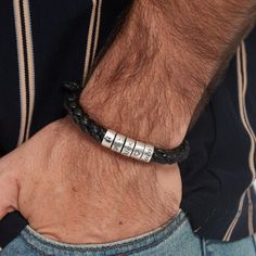 a man wearing a black leather bracelet with two silver beads on it's wrist