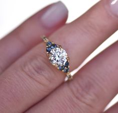 a woman's hand with a diamond and blue sapphire engagement ring on her finger