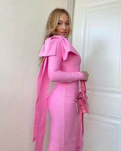 a woman in a pink dress is leaning against a wall and posing for the camera