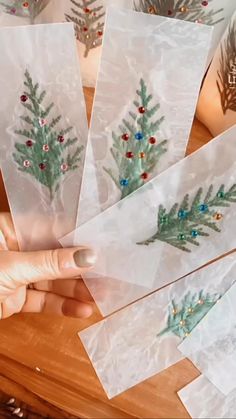 someone is holding up some christmas cards on a table with pine cones and holly branches