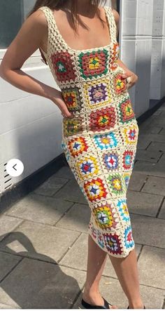 a woman in a crocheted dress is standing on the sidewalk with her hands on her hips