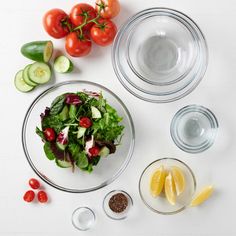 the ingredients to make a salad laid out on a white surface including tomatoes, cucumbers, lemons and lettuce