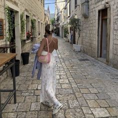 a woman walking down an alley way carrying a pink purse