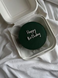 a green birthday cake in a white container on a bed with the words happy birthday written on it