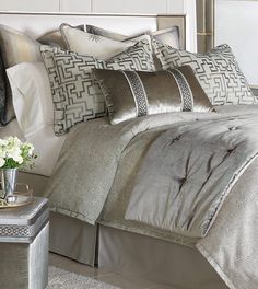 a bed with silver sheets and pillows on top of it next to a night stand