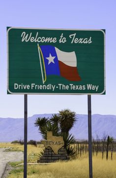 a welcome to texas sign in front of a field with palm trees and mountains behind it