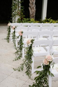 rows of white chairs decorated with flowers and greenery