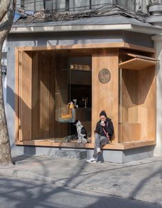 a man sitting in front of a display case with two dogs on the sidewalk next to it