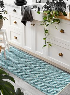 a kitchen with white cabinets and green plants in pots on the counter top next to a blue rug