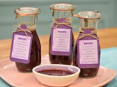 three jars of jam sit on a plate with a small bowl of sauce next to it