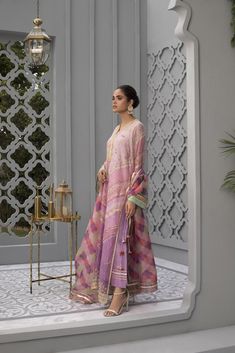 This long cotton net printed shirt in shades of pinks with contrasting embellished chevrons features intricate detailing. It is paired with rawsilk trousers and a geometric printed organza dupatta. Designer Pink Lawn Suit With Printed Motifs, Unstitched Pink Silk Lawn Suit, Designer Pink Silk Lawn Suit, Pink Chanderi Lawn Suit With Long Sleeves, Pink Silk Lawn Suit Designer Wear, Pink Silk Lawn Suit For Designer Wear, Pink Chanderi Lawn Suit With Printed Motifs, Pink Lawn Suit With Printed Motifs For Festive Occasions, Festive Pink Lawn Suit In Cotton Silk