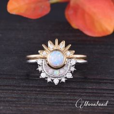 a white opal and diamond ring sitting on top of a wooden table next to an orange flower