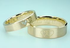 two gold wedding rings with hearts and names engraved on the sides, set against a blue background