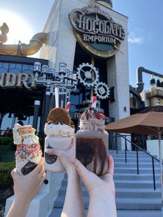 two people holding up drinks in front of a chocolate emporant shop with stairs