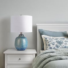 a blue vase sitting on top of a bed next to a night stand with a lamp