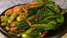 a black bowl filled with green vegetables covered in sauce