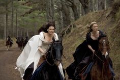 two women dressed in medieval clothing riding horses down a path with other people on horseback behind them