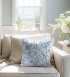 a blue and white pillow sitting on top of a couch next to a vase with flowers