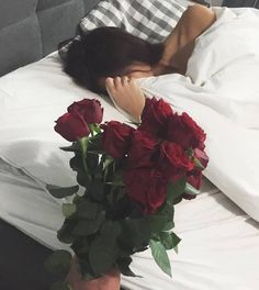 a woman laying in bed with her head on the pillow next to a bouquet of roses