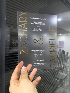 a person holding up a silver and gold foiled card in front of a window