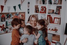 a woman is hugging her children while they are all in the same room with bookshelves and pictures on the wall