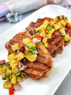 two grilled pork chops with pineapple salsa on a white plate next to a fork