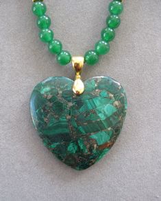 Pretty Small Heart Malachite Pendant Necklace with Malachite beads and gold accents.   It measures 1 1/2 inches by 1 1/2. The necklace is heart shaped and the beads in the necklace are malachite. The necklace is 16 inches and adjustable to 21 inches with Lobster clasp.  The stone is polished. It will go with anything. This is a unique one of a kind necklace.  It comes with a certificate describing the stone. All my jewelry is unique and one of a kind. Similar quality jewelry is priced at double. I source the stone pendants from all over the world. All pendants and necklaces are made with semiprecious stones and beads. I spend hours coordinating the pendants with the semiprecious stone, pearls or crystal beads. Many of the stones are crazy lace agate, dragon vein agate, agate, malachite, ja Green Heart-shaped Beaded Necklace Gift, Spiritual Green Jewelry With Heart Beads, Spiritual Green Heart Beads Jewelry, Green Heart-shaped Natural Stone Jewelry, Green Heart Beads Pendant Necklace, Green Jewelry With Heart Charm And Round Beads, Heart-shaped Green Necklace With Heart Beads, Green Heart Necklace With Heart Beads, Green Heart-shaped Necklace With Heart Beads