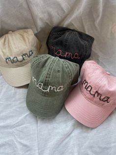 four hats with the word mama on them are lined up against a white bed sheet