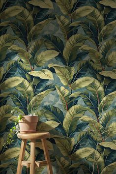 a plant sits on a stool in front of a wallpapered with green leaves