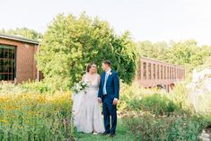 a bride and groom standing in front of a brick building with wildflowers on the lawn