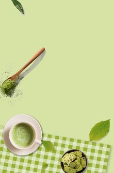 a cup of green tea next to a spoon on a checkered tablecloth with leaves