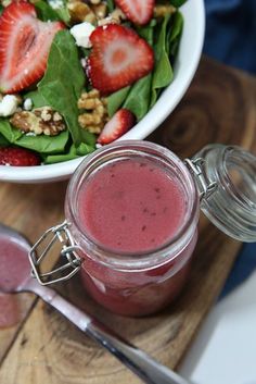 a salad with strawberries and spinach is in a jar next to a spoon